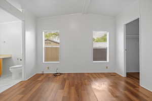 Unfurnished bedroom with wood finished floors, a walk in closet, a closet, and connected bathroom