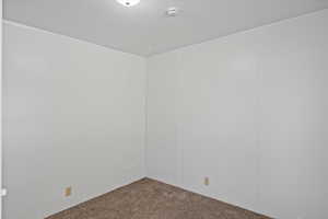 Carpeted empty room with a smoke detector and a textured ceiling