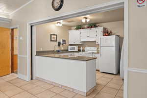 Kitchen with white appliances, ornamental molding, a sink, light tile patterned floors, and white cabinetry