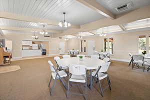 Carpeted dining area with a chandelier, beam ceiling, and baseboards