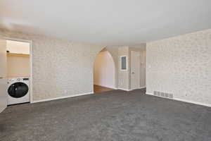 Spare room with washer / dryer, dark carpet, arched walkways, wallpapered walls, and electric panel