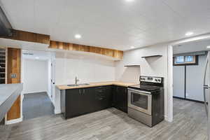 Kitchen with stainless steel range with electric cooktop, dark cabinets, a sink, light wood-style floors, and open shelves