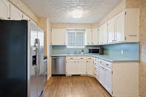 Kitchen with appliances with stainless steel finishes, light wood-type flooring, a sink, white cabinetry, and a textured ceiling
