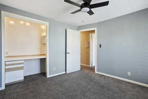 Unfurnished bedroom featuring dark carpet, baseboards, and ceiling fan