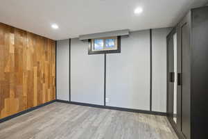 Basement with light wood finished floors, recessed lighting, and wood walls