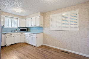 Kitchen featuring light wood-type flooring, appliances with stainless steel finishes, white cabinets, and a textured ceiling
