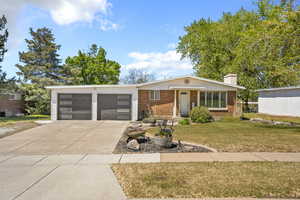 View of front facade featuring concrete driveway, a front lawn, an attached garage, a chimney, and brick siding