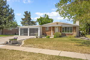 View of front of property with brick siding, driveway, a garage, a front yard, and a chimney