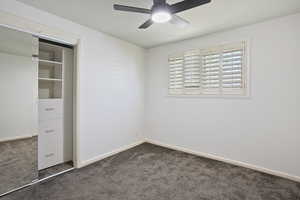 Unfurnished bedroom with dark carpet, baseboards, and a ceiling fan