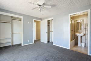 Unfurnished bedroom featuring a textured ceiling, carpet floors, connected bathroom, a ceiling fan, and baseboards