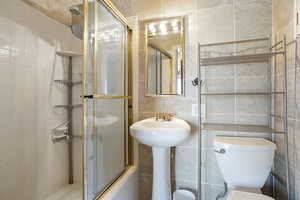 Full bath with tile walls, a stall shower, toilet, and a sink