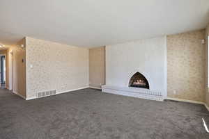 Unfurnished living room with dark colored carpet, a large fireplace, and wallpapered walls