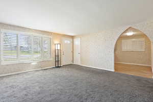 Unfurnished living room featuring wallpapered walls, carpet floors, and baseboards