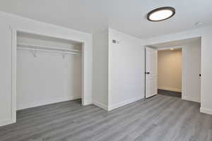 Unfurnished bedroom featuring wood finished floors, a closet, baseboards, and a textured ceiling