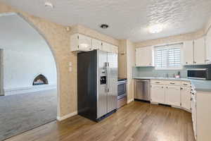 Kitchen featuring stainless steel appliances, arched walkways, light wood-style floors, white cabinets, and light countertops