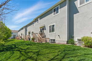 Rear view of house featuring stucco siding, a lawn, stairs, and a residential view