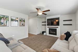 Carpeted living area featuring ceiling fan, baseboards, and a fireplace
