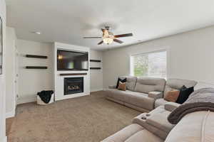 Living area featuring ceiling fan, baseboards, a large fireplace, carpet floors, and a textured ceiling