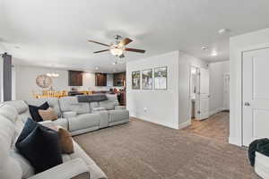 Living room with light carpet, a ceiling fan, a chandelier, and baseboards