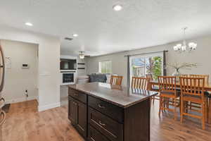 Kitchen featuring a ceiling fan, light wood finished floors, a glass covered fireplace, a textured ceiling, and a chandelier