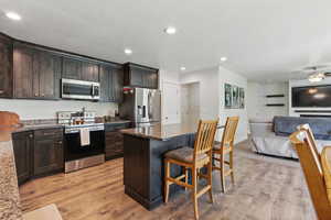 Kitchen with stainless steel appliances, a breakfast bar, dark stone countertops, open floor plan, and light wood-type flooring