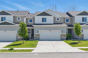 Townhome / multi-family property with stone siding, driveway, a front lawn, and a garage