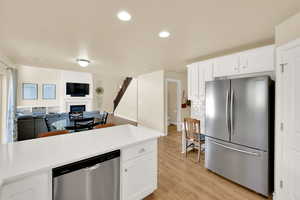 Kitchen featuring stainless steel appliances, light wood-style flooring, light countertops, white cabinets, and open floor plan