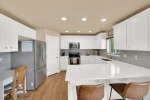 Kitchen with stainless steel appliances, a sink, a peninsula, tasteful backsplash, and light wood-style floors