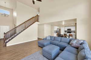 Living area with a towering ceiling, stairway, light wood-type flooring, ceiling fan, and a chandelier