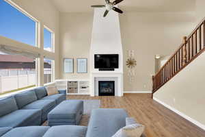 Living room with a high ceiling, a ceiling fan, stairs, light wood finished floors, and baseboards