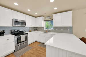 Kitchen featuring stainless steel appliances, a sink, a peninsula, light countertops, and light wood finished floors