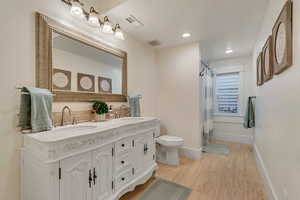 Full bathroom with toilet, baseboards, curtained shower, double vanity, and recessed lighting