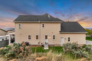 Rear view of house featuring fence, entry steps, and roof with shingles