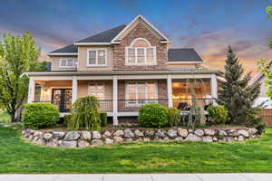 View of front of home with stone siding, a yard, covered porch, and roof with shingles
