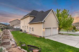 Property exterior at dusk featuring driveway, a shingled roof, and a garden