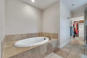 Bathroom featuring a spacious closet, a garden tub, and baseboards