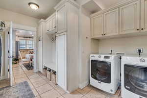 Laundry area with separate washer and dryer, cabinet space, stone tile flooring, and baseboards