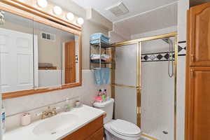 Full bath with a shower stall, vanity, toilet, and tile walls