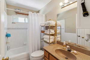 Full bathroom featuring toilet, shower / tub combo with curtain, tile walls, vanity, and wainscoting
