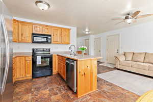 Kitchen featuring black appliances, a sink, a peninsula, open floor plan, and stone tile flooring