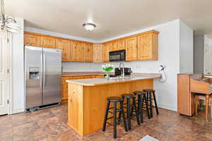 Kitchen with black appliances, stone finish flooring, a peninsula, a kitchen bar, and baseboards