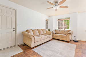 Living room with ceiling fan, stone tile flooring, and baseboards