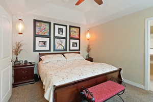 Bedroom featuring carpet floors, a tray ceiling, baseboards, ceiling fan, and connected bathroom