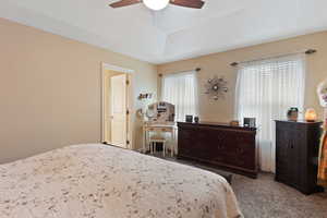 Carpeted bedroom featuring a ceiling fan and a tray ceiling
