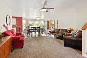 Carpeted living area with a ceiling fan, a textured ceiling, and baseboards