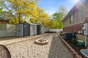 Fenced backyard featuring an outdoor fire pit, a storage unit, cooling unit, an outbuilding, and a patio area