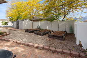 Fenced backyard with a vegetable garden, a storage unit, and an outbuilding