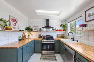 Kitchen featuring a sink, wall chimney range hood, wood counters, open shelves, and appliances with stainless steel finishes