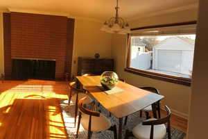 Dining area with crown molding, a fireplace, a chandelier, and wood finished floors