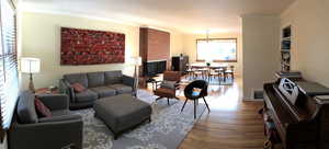 Living room featuring wood finished floors, ornamental molding, a chandelier, baseboards, and a brick fireplace